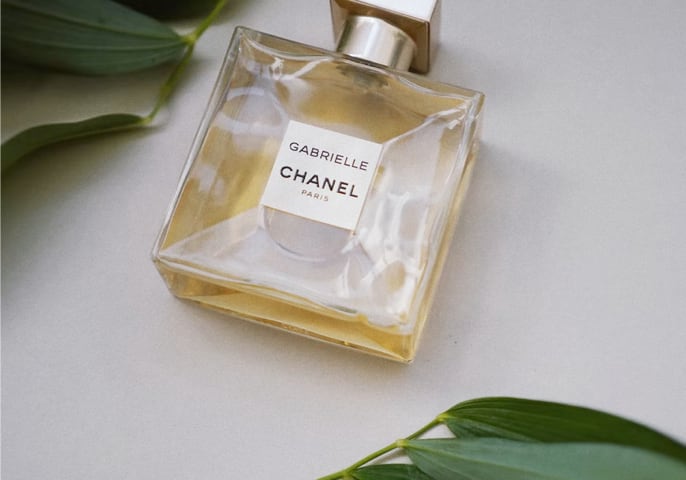 
    A bottle of Chanel Gabrielle perfume placed on a light surface, surrounded by green leaves